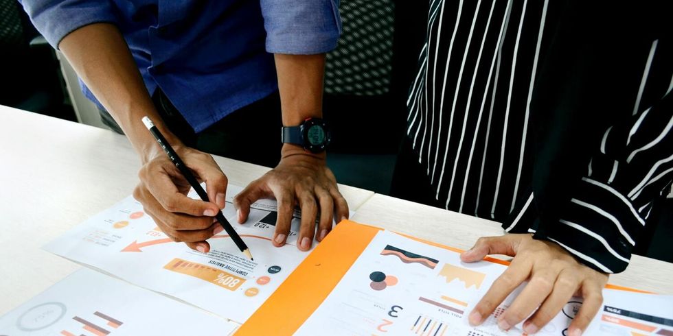 Zwei Personen haben Datensätze auf dem Schreibtisch ausgebreitet und werten diese zusammen aus.