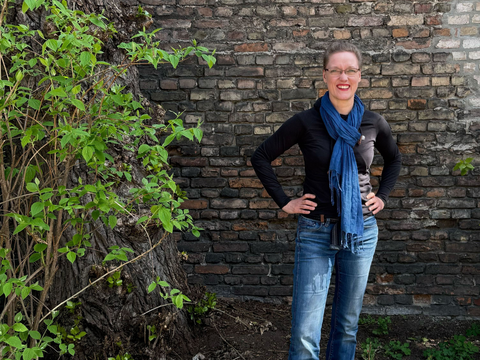 Frau Wittmer steht vor einer Mauer neben einer begrünten Fläche.