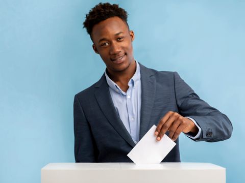 junger Mann im Anzug steckt Umschlag in eine Wahlurne