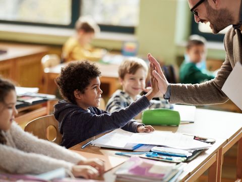Happy teacher and schoolboy giving each other high-five on a class.