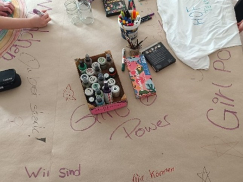 Der Boden ist mit Papierfolie bedeckt und darauf Stifte und handgeschriebene Aussagen zum Internationalen Frauentag