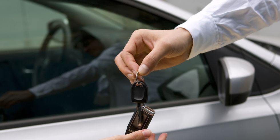 Mann gibt Frau einen Autoschlüssel in die Hand, im Hintergrund ein Auto