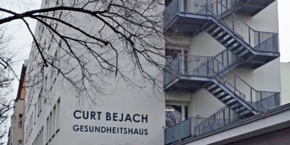 Mehrstöckiges Gebäude mit außenliegender Treppe und Schriftzug 'CURT BEJACH GESUNDHEITSHAUS' an der Fassade