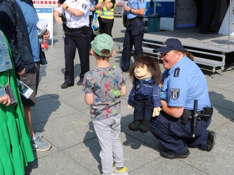 Knieende Polizistin mit einer Puppe vor einem Kind und Eltern