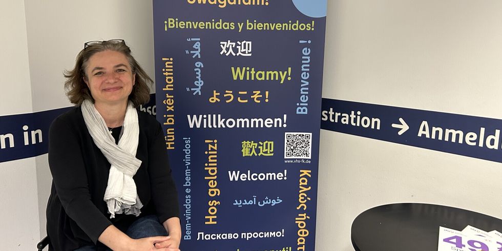 Vor einem Banner, auf dem "Willkommen!" in verschiedenen Sprachen steht, sitzt eine Frau.