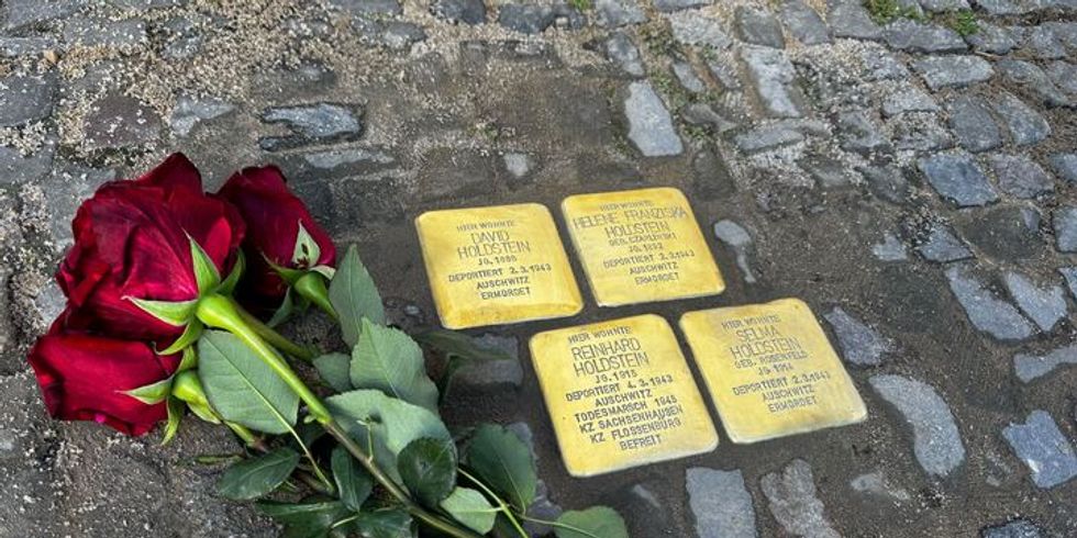 Rote Rosen auf Pflastersteinen neben Stolpersteinen