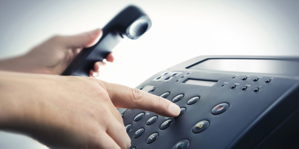 Eine Hand wählt eine Rufnummer auf dem Telefon