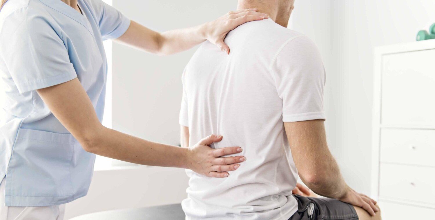 Ärztin tastet Patient mit Rückenschmerzen am Rücken ab