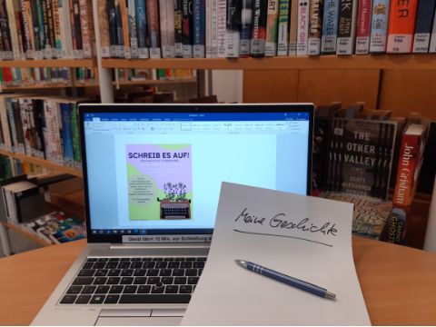 aufgeschlagener Laptop in einer Bibliothek mit einem Blatt darauf: Meine Geschichte