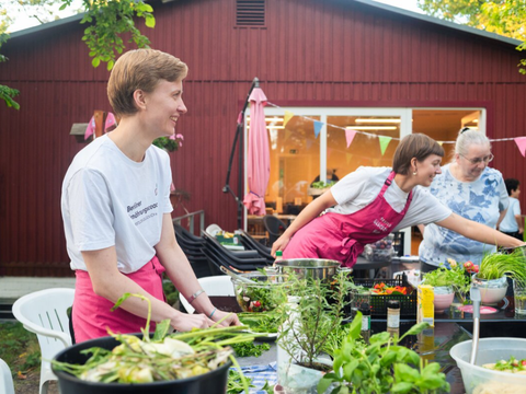 Drei Frauen stehen an einem Tisch und schneiden Kräuter und Gemüse