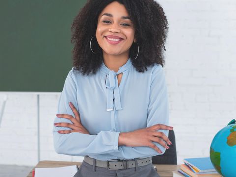 Afikanische Lehrerin lehnt lächelnt am Lehrerpult