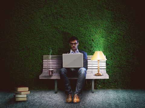 Junger Mann mit aufgeklapptem Notebook auf einer Parkbank sitzend.