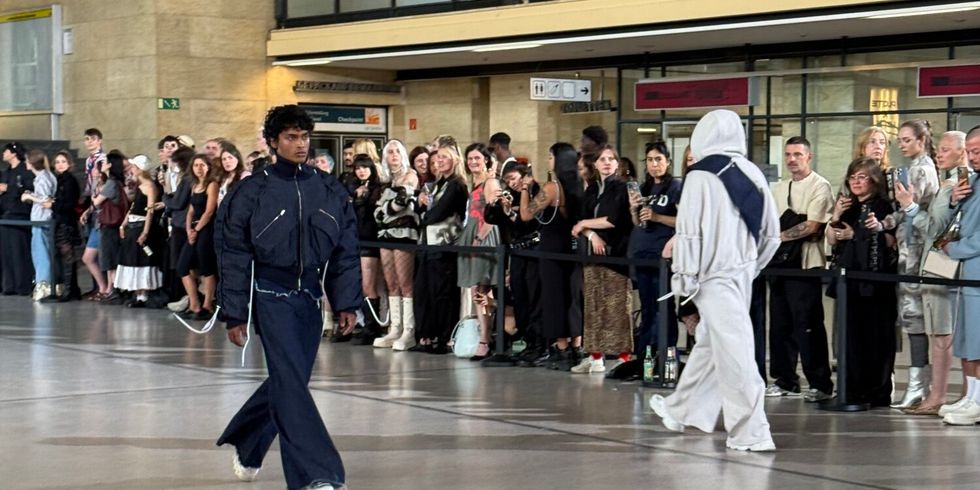 Zwei Models laufen in einer großen Halle. Viele schauen zu.