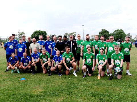 Zwei Fußballmannschaften mit Schiedsrichtern präsentieren sinch vor der Kamera.