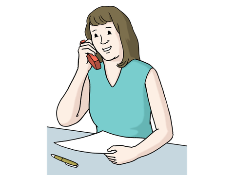 Frau telefoniert. Vor ihr liegen Zettel und Stift auf dem Tisch