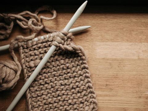 Auf einem tisch liegt ein angefangenes Strickprojekt mit zwei Stricknadeln und hellbrauner Woller