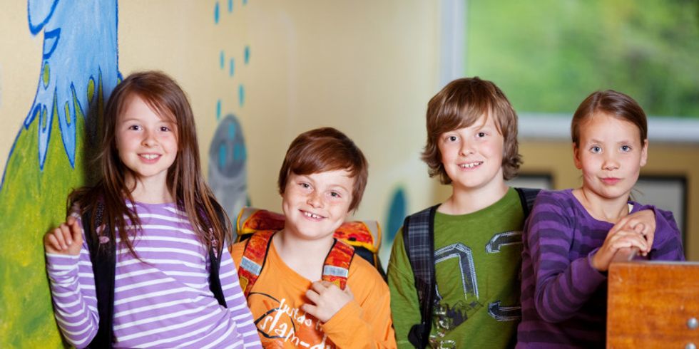 Zwei Mädchen und zwei Jungen stehen vor einer bemalten Wand in einer Schule