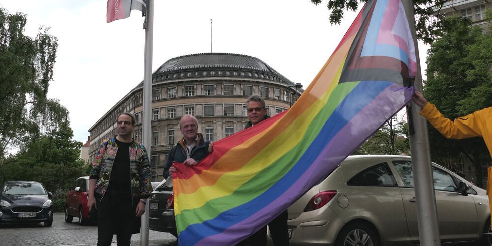 Drei Männer stehen neben einem Fahnenmast und halten eine Flagge hoch.