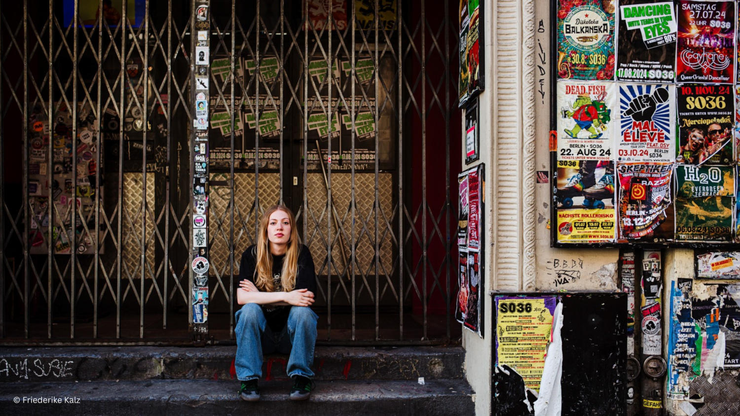 Fotografie der Musikerin Emmo, die auf den Stufen eines Häusereingangs sitzt