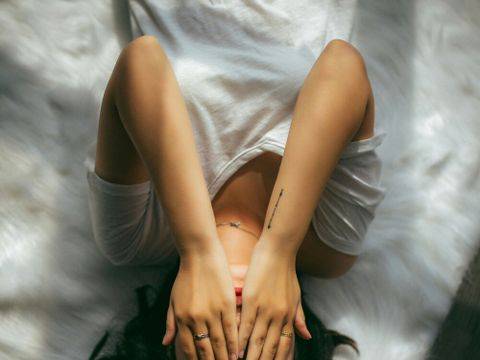 Frau liegt auf einem Bett und hält sich die Hände vors Gesicht