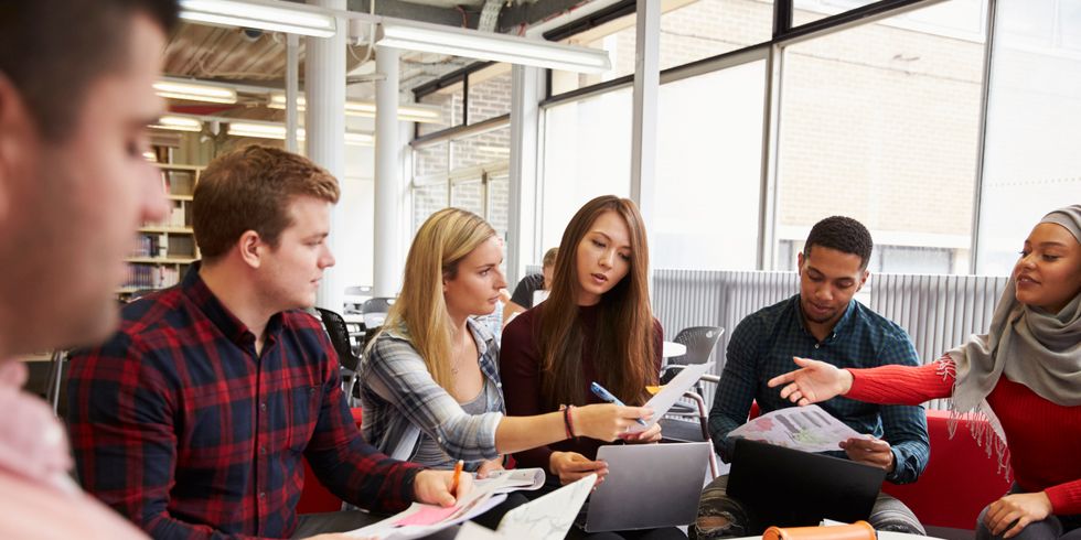 Gruppe Studenten sitzt an einem runden Tisch und macht Projektarbeit