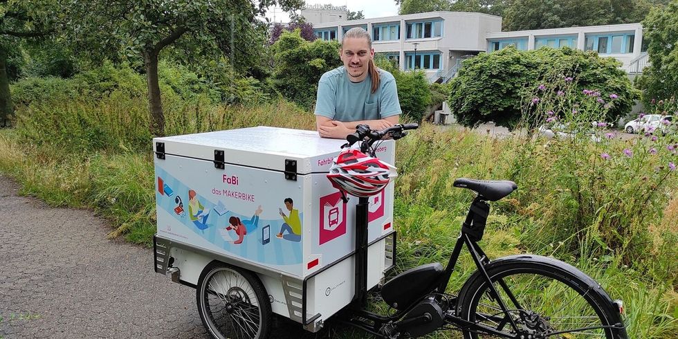 ein Mann steht mit einem Lastenfahrrad in einer Grünanlage