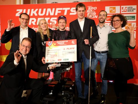 Sieben Menschen nehmen einen Preis entgegen. Eine Person sitzt im Rollstuhl, eine weitere trägt einen Blindenstock