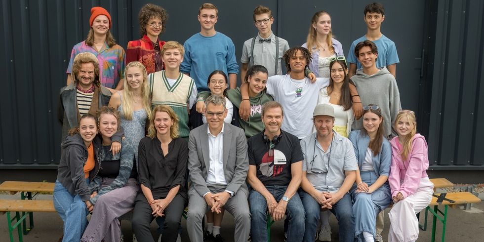 Mehrere Personen stehen und sitzen in drei Reihen und schauen in die Kamera.