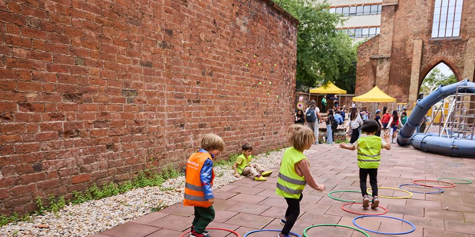 Kinder in Warnwesten springen in bunte Reifen