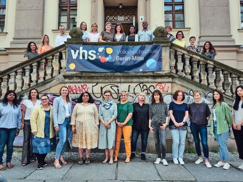 Gruppenfoto von etwa 25 Personen vor einem Gebäude mit Treppe und dem Banner der Volkshochschule (VHS). Die Menschen stehen und sitzen auf der Treppe und davor.