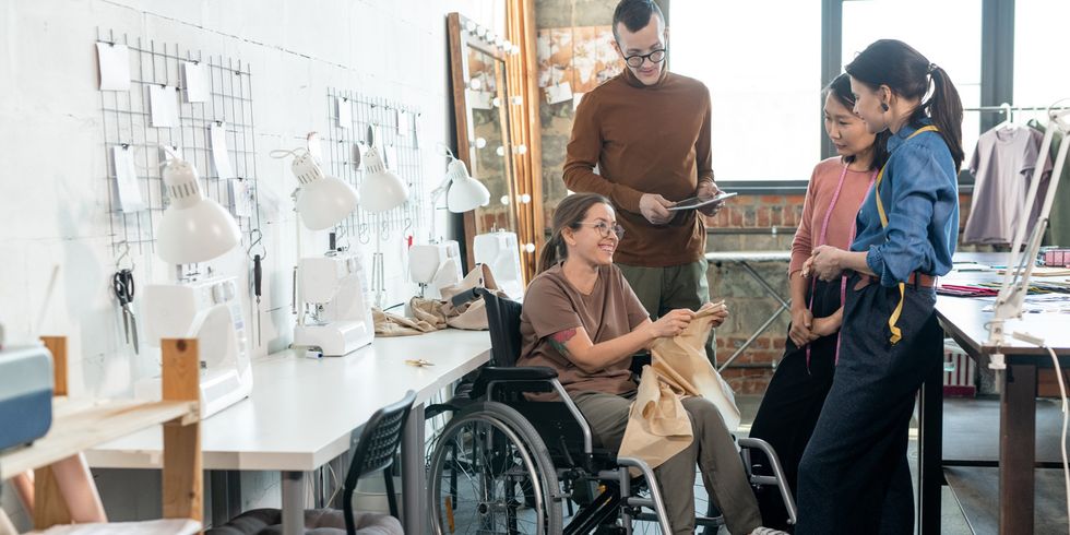 Ein Team in einer Nähwerkstatt bespricht sich. Eine Frau nutzt einen Rollstuhl.