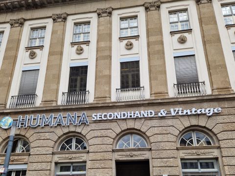 Fassadenansicht vom Humana Secondhand und Vitage Laden mit Postern in den Erdgeschossfensern und vor der Tür
