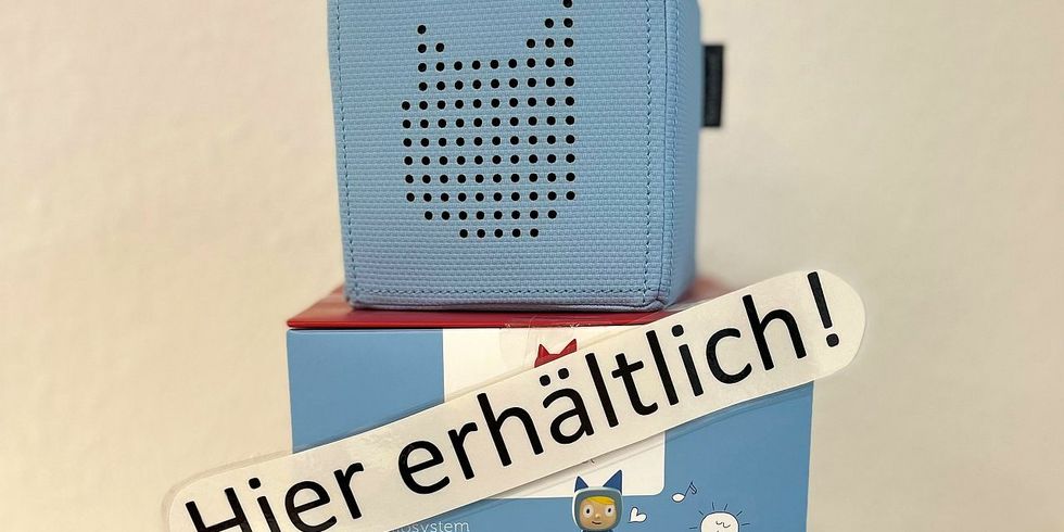 Das Bild zeigt eine hellblaue Tonie-Box mit dem Schild "Hier erhältlich!" und verschiedenen Tonie-Figuren in der Mittelpunktbibliothek Ehm Welk