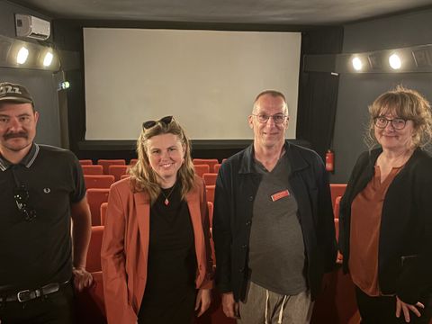 Vier Personen stehen in einem kleinen Kinosaal mit roten Stühlen vor einer weißen Leinwand. Von links nach rechts: Manuel Godehardt vom Kino Intimes, Bezirksbürgermeisterin Clara Herrmann, Frank Hüpperling (FKU-Vorstand) und Kathrin Klisch von der Wirtschaftsförderung des Bezirksamts Friedrichshain-Kreuzberg. Alle blicken freundlich in die Kamera, das Licht im Saal ist gedimmt, aber die Gesichter sind gut zu erkennen.