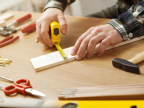 Mann sitzt an Werkbank und vermisst ein Stück Holz