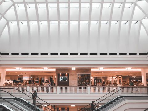 Innenaufnahme eines Einkaufszentrums mit einer Rolltreppe und Geschäften verteilt auf verschiedenen Ebenen.