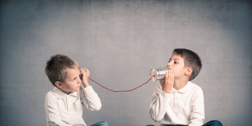 Zwei Jungs telefonieren, indem sie Blechbüchsen an ihre Ohren halten.
