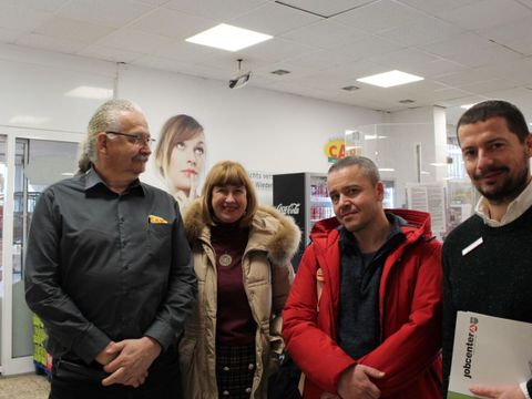 Eine Gruppe von vier Menschen stehen zusammen in einem Supermarkt und schauen freundlich in die Kamera.