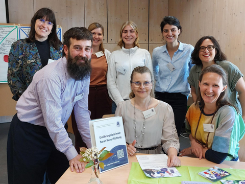 Acht erwachsene Menschen lächeln in die Kamera, auf einem Tisch vor ihnen liegen Flyer der Sarah Wiener Stiftung