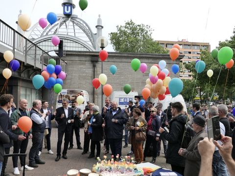 Viele Menschen stehen auf einem Platz und halten Luftballons an Schnüren.