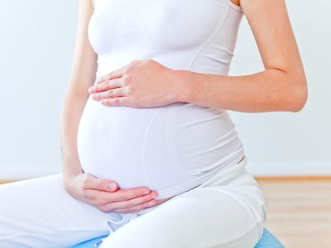 Schwangere Frau umfasst ihren Bauch mit den Händen