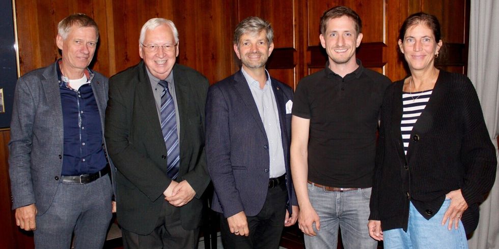 Vier Männer und eine Frau stehen nebeneinander in einem Raum und lächeln in die Kamera.