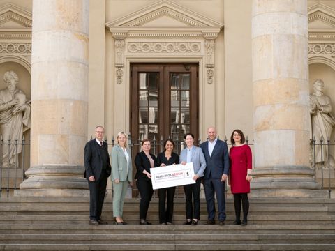 7 Ministerinnen und Minister stehen auf den Stufen des Französischen Dom und halten ein Schild mit der Aufschrift VSMK 2025 in den Händen