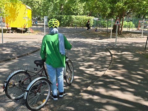 Eine Frau versucht sich während ihrer ersten Fahrstunde zunächst auf einem Dreirad für erwachsende Fahrer*innen bevor sie auch auf zwei Rädern das Fahren versucht