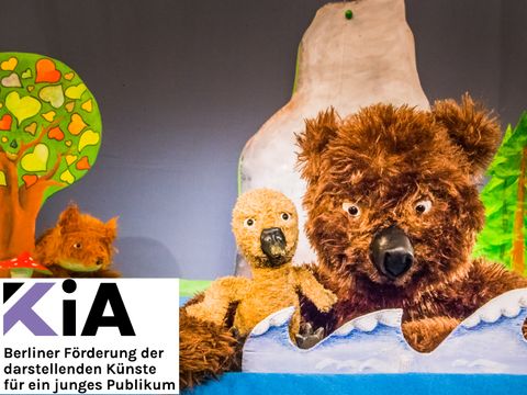 Zwei Stofftiere - ein Bär hällt eine Ganz / Logo: KiA
