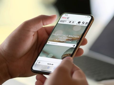 Hände halten ein Handy mit Startseite des Karriereportals
