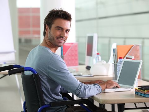 Junger Rollstuhlfahrer sitzt am Schreibtisch