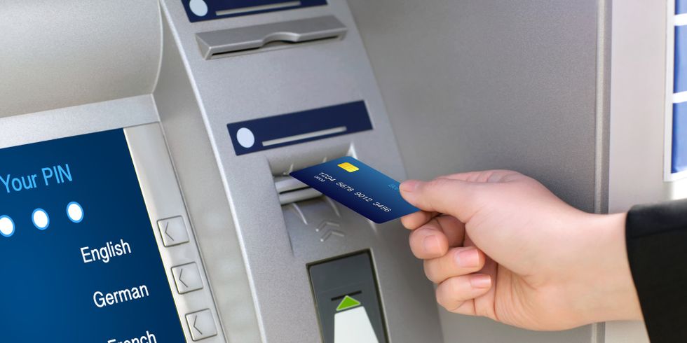 Jemand schiebt eine Bankkarte in einen Geldautomaten, auf dem Display kann zwischen verschiedenen Sprachen gewählt werden