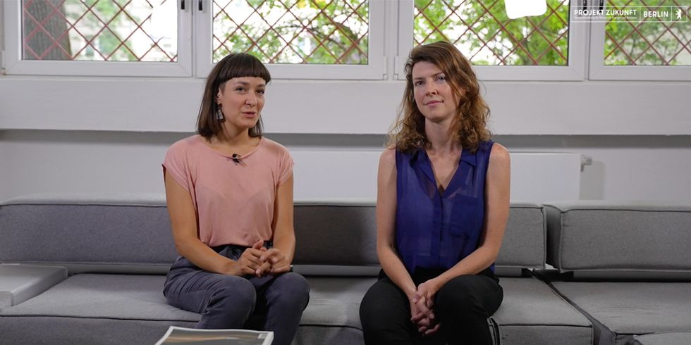 Mitgründerinnen von macht.sprache schauen frontal in die Kamera und sitzen auf einer grauen Couch