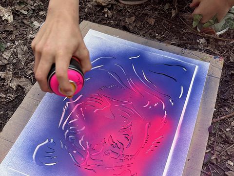 Kreativ Labor: Kind sprüht Farbe über Schablone auf einem Papierbogen (Bild: © Christoph Vieweg)